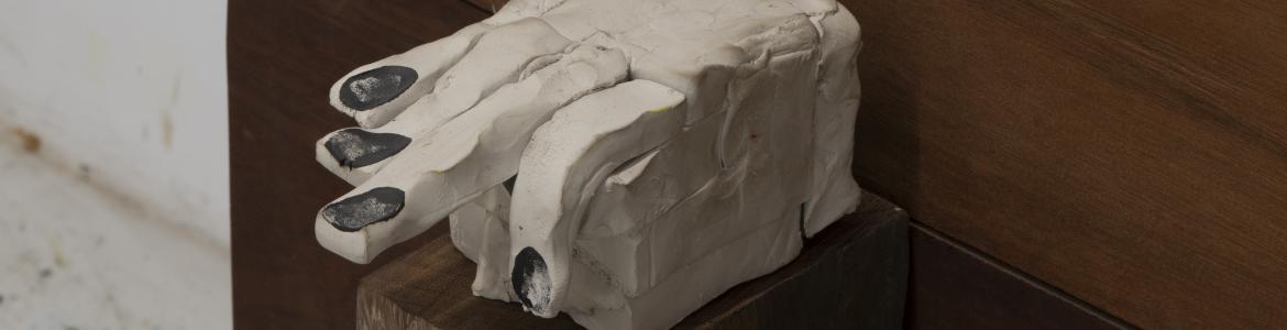 Imagen de una mano en escayola blanca sobre un banco de madera oscuro