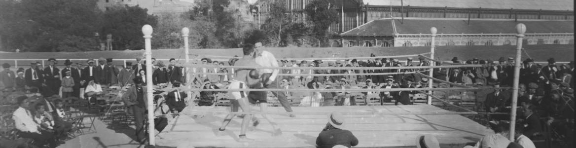 Foto en blanco y negro con un ring de boxeo y público observando el espectáculo