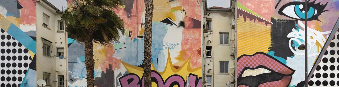 Street of a city with buildings with graffiti, palm trees and red car