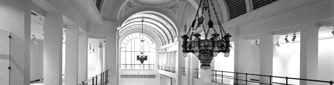 Vista en blanco y negro de la bóveda de cristal, lámpara y sala de exposiciones de la Consejería de Cultura