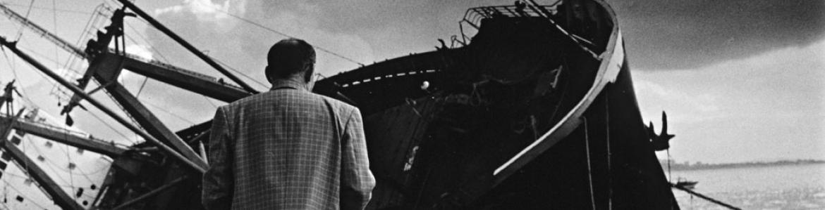 Imagen en blanco y negro con un hombre de espadas andando hacia un barco hundido