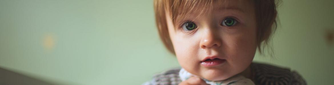 Niño de frente agarrado a muselina asomado a una barandilla