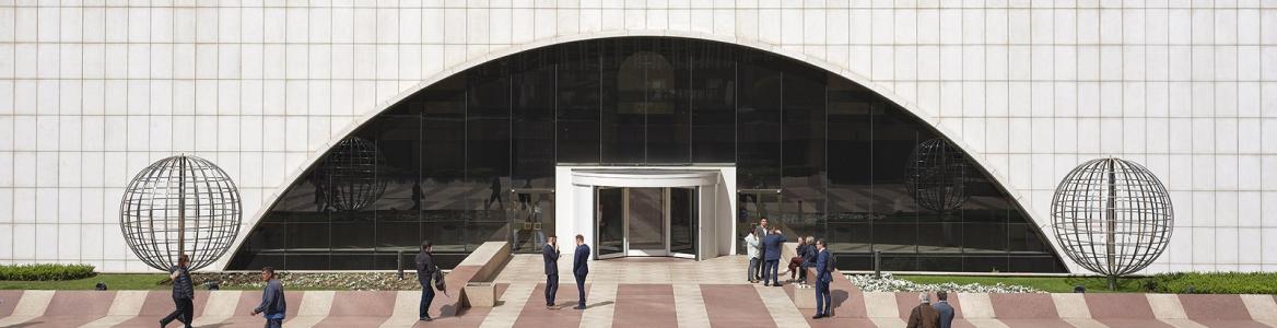 Varias personas andando en una plaza, se aprecia la entrada y parte inferior del edificio Torre Picasso