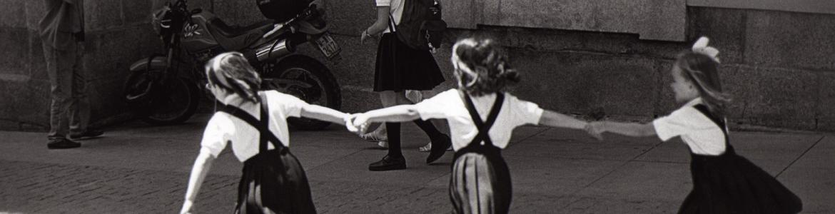 Tres niñas vestidas con uniforme, de espaldas, jugando en la calle