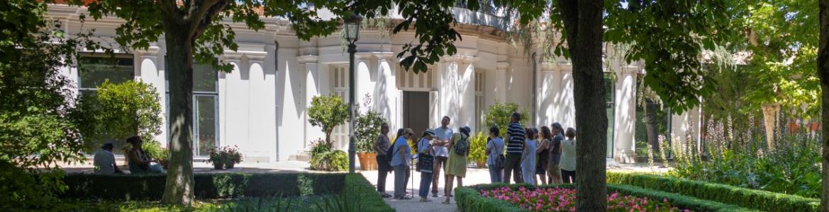 grupo de personas de espaldas en una visita guiada en un jardín con edificio al fondo