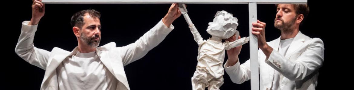 imagen de dos hombres vestidos de color blanco sujetando un títere de un niño todo color blanco
