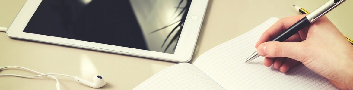 tablet, cuaderno y unas manos escribiendo en el cuaderno