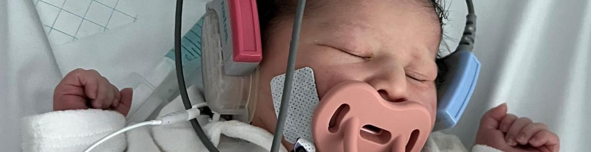 recién nacida con sensores y cascos en los oídos dormida