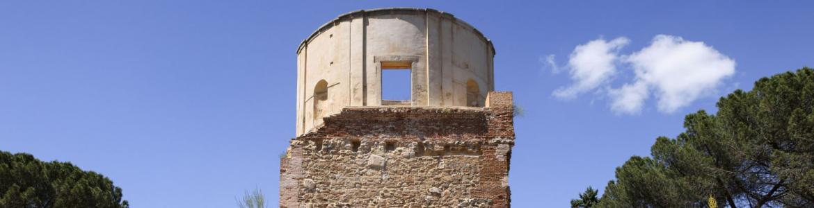 edificio con torreón semicircular y perímetro de piedra con un campo de amapolas en primer plano