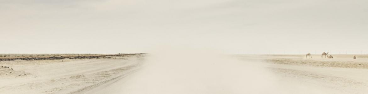Photography with warm colors showing a desert road and full of dust in suspension