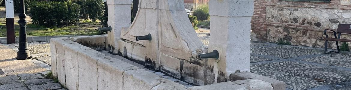 Fuente de piedra blanca con un pilón de agua, dos columnas y un escudo central con inscripciones