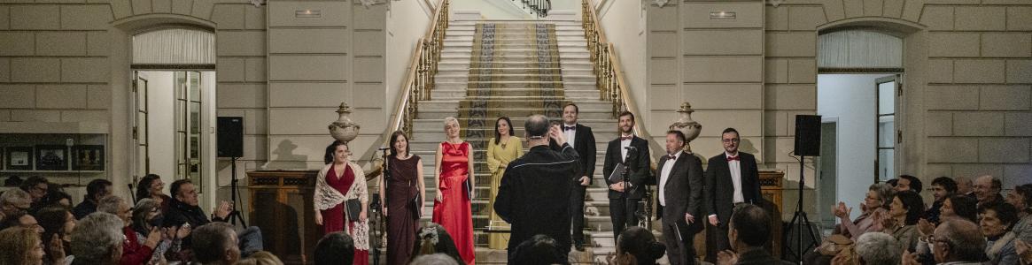 A choir and its conductor at a concert with an audience inside a palace