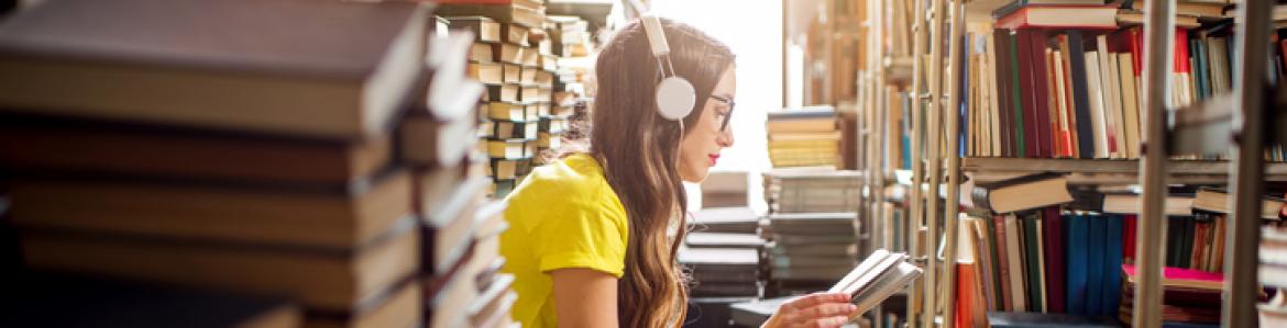 Girl with long hair and glasses sitting among stacks of books