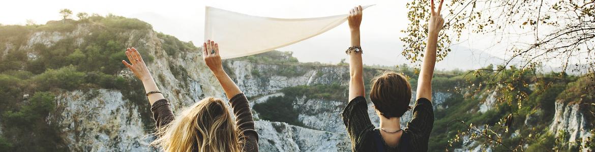 Dos chicas de espaldas levantando un pañuelo en paisaje de montaña
