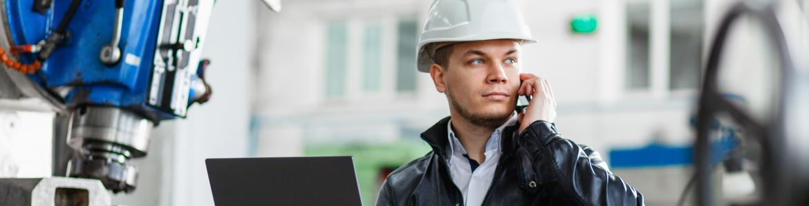 Industrial machinery operator talks to the mobile while holding a laptop