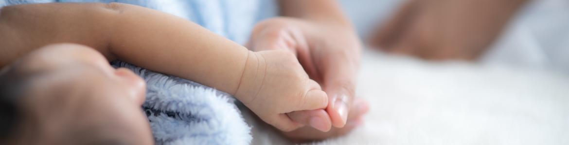 Plano de detalle de un adulto dando la mano a un bebe tumbado y tapado con una manta