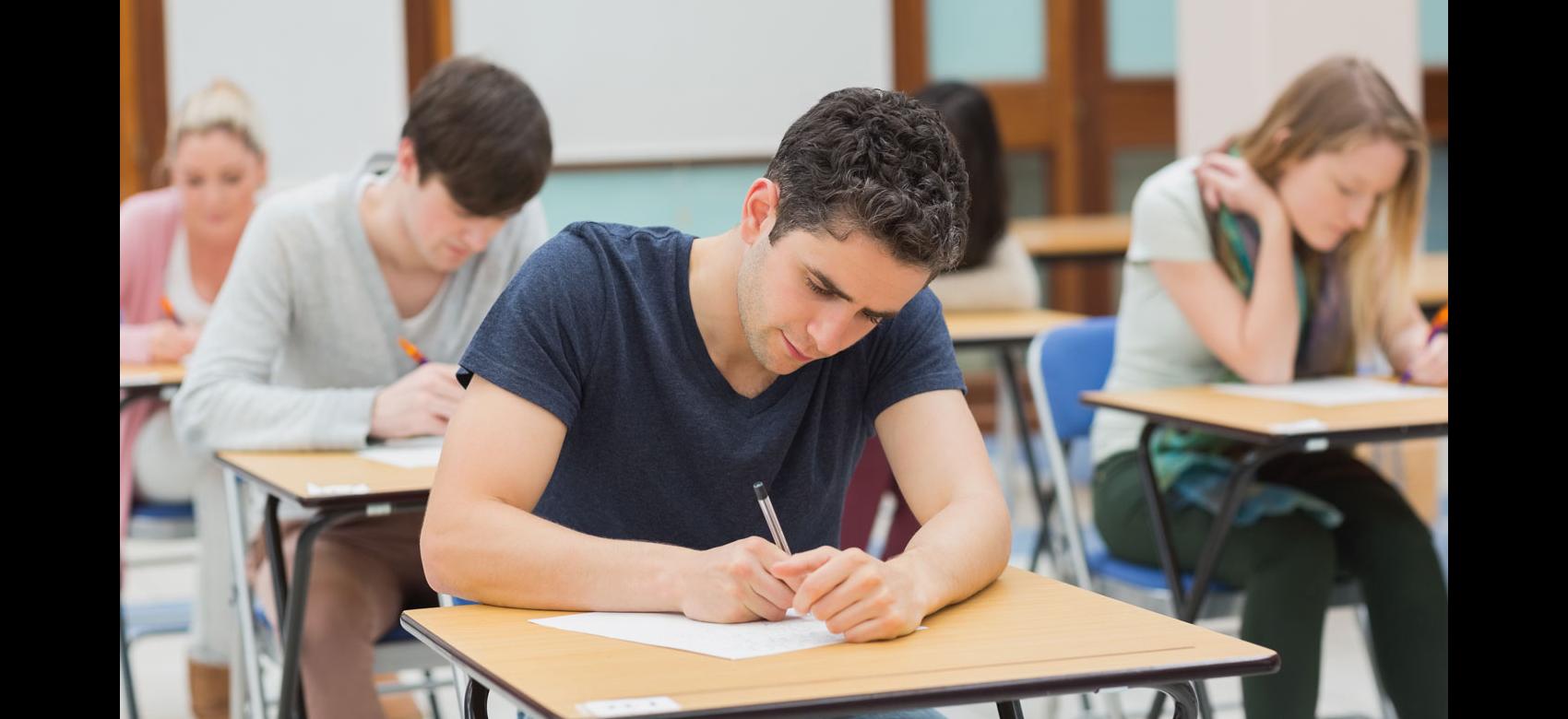 Chico joven inclinado sobre una mesa mientras escribe en una hoja de examen
