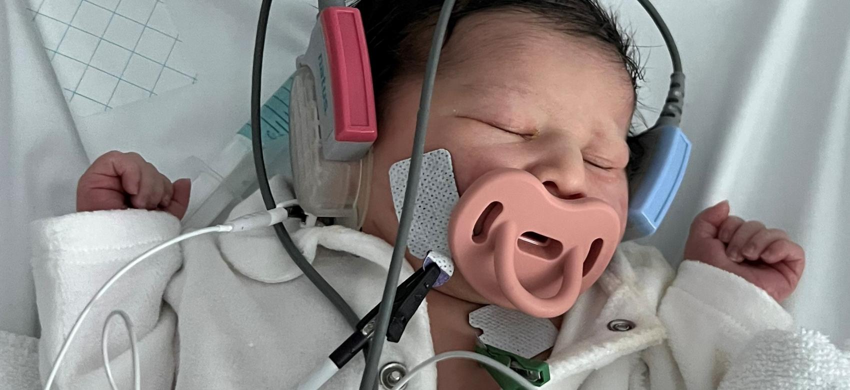 recién nacida con sensores y cascos en los oídos dormida