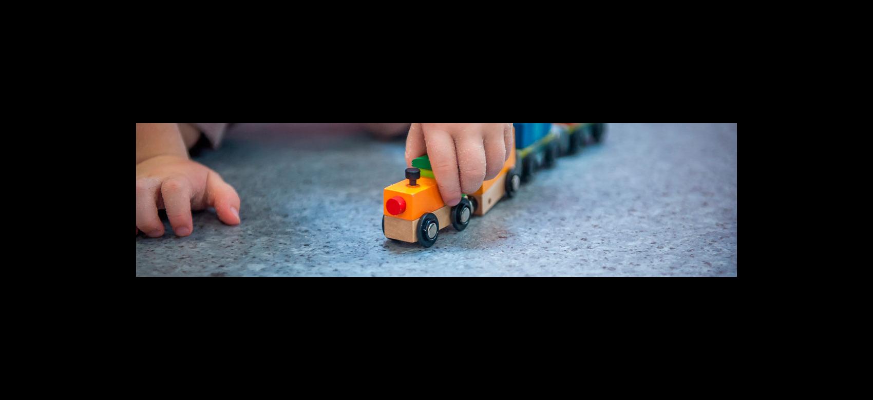 Detalle de la mano de un bebé que juega con un tren de madera