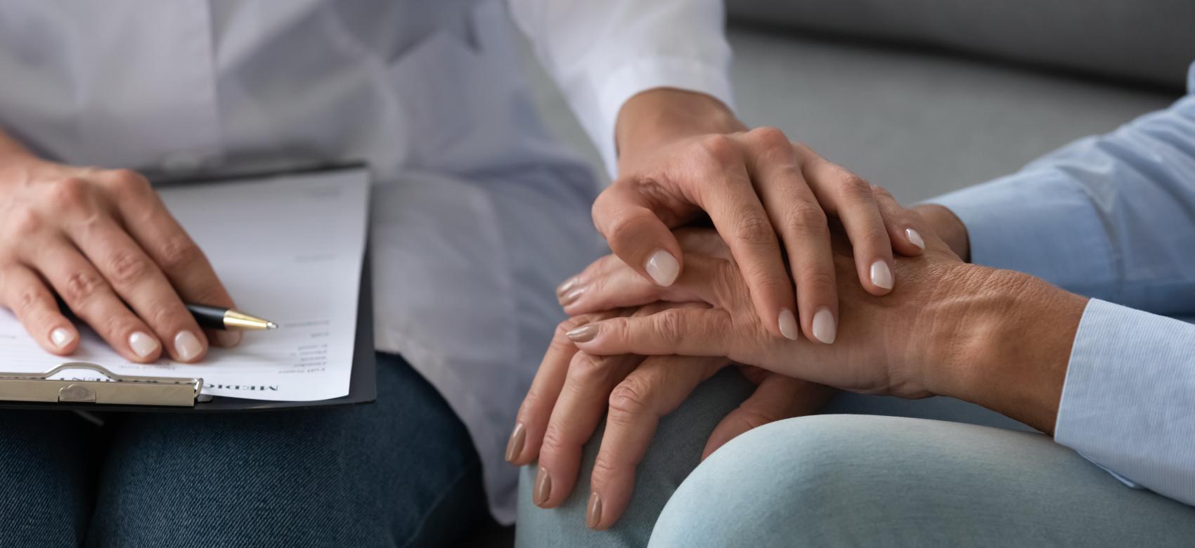 Cabecera manos Una persona muestra su apoyo a otra colocando su mano sobre las suyas al tiempo que toma notas en una libreta