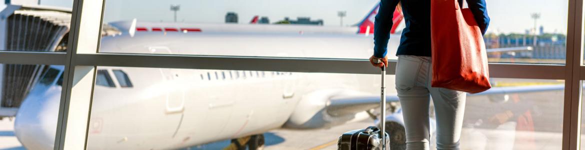 Mujer de espaldas mirando un avión desde las ventanas de la terminal del aeropuerto