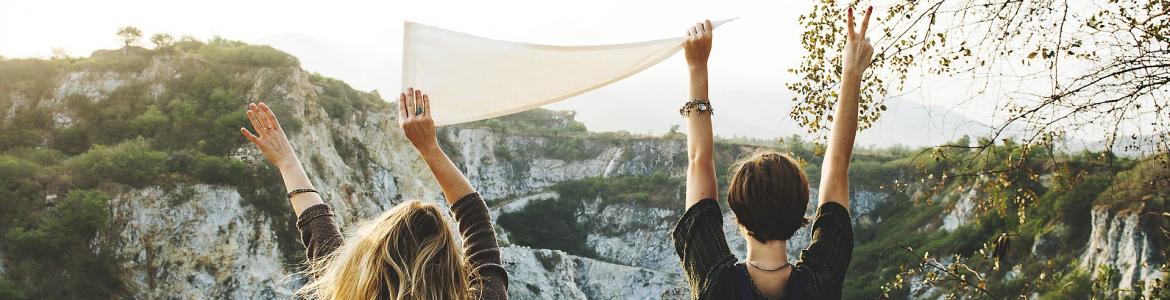 Dos chicas de espaldas levantando un pañuelo en paisaje de montaña