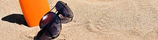 Gafas de sol y envase de crema protectora sobre arena de playa