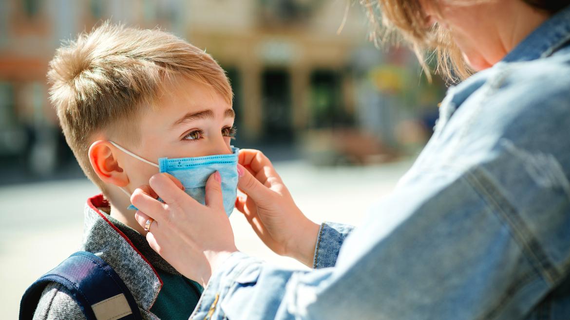 Una mujer le pone una mascarilla a un niño