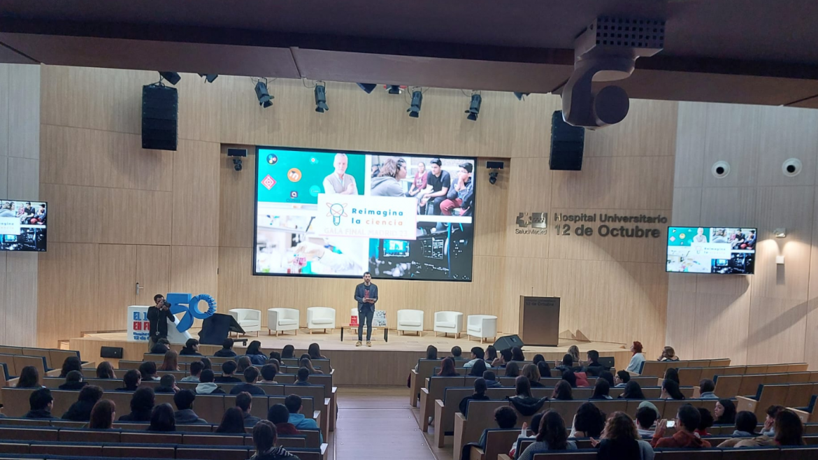 Imagen del Auditorio del Hospital 12 de Octubre durante la celebración de la gala Reimagina la ciencia escenario al fondo y varias filas de butacas visto desde atrás.