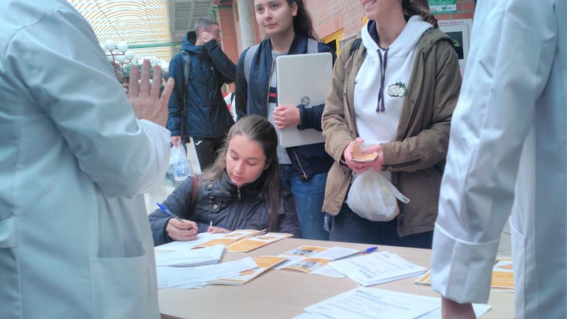 Alumnos reciben información en una mesa con folletos atendida por una enfermera en el hall de una facultad