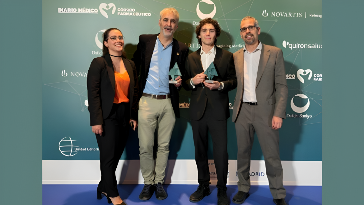 Posado en escenario fondo verde tres hombres y una mujer a la izquierda y los del medio con premio en la mano