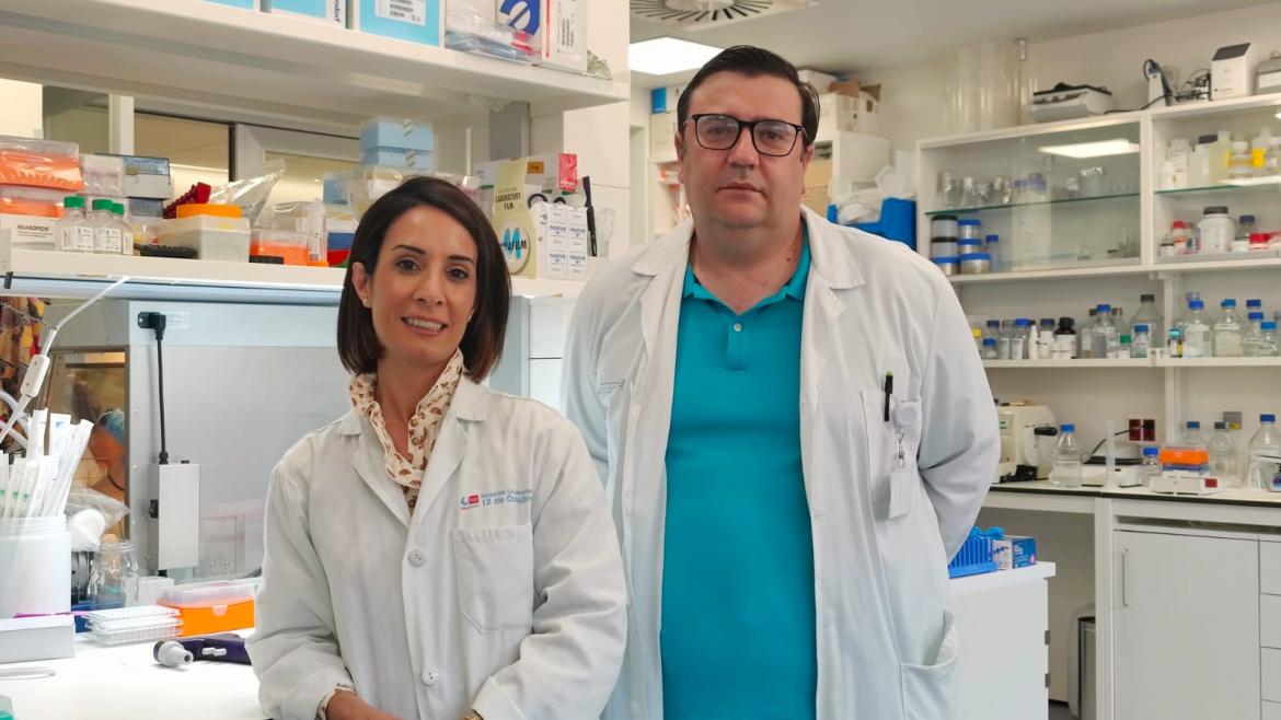 Una médica y un médico, ambos con bata, posando delante del laboratorio