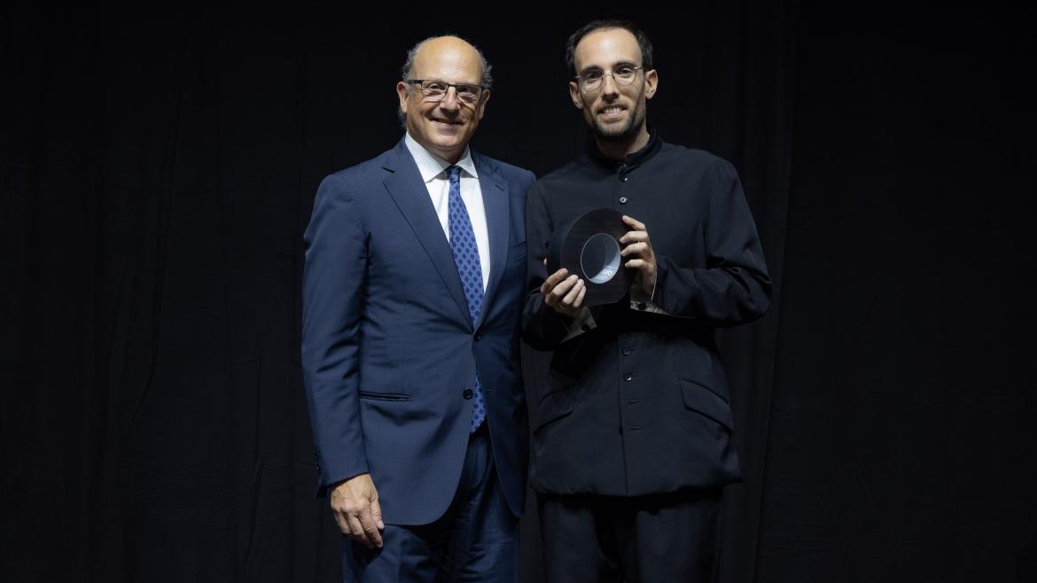hombre con traje azul oscuro recibiendo un premio sobre un fondo azul oscuro