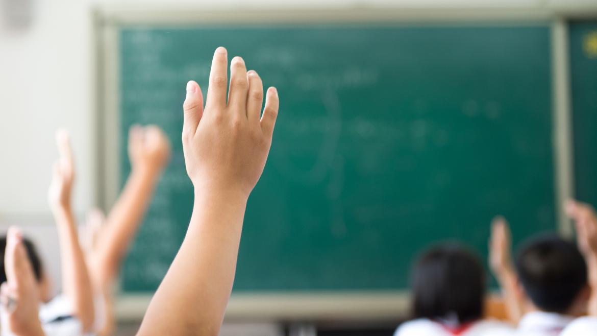 Unos niños en un aula de clases piden permiso para hablar con la mano levantada