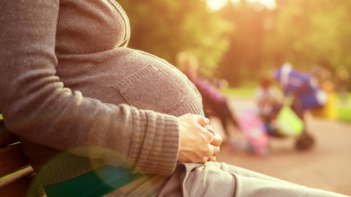 Una joven embarazada toca su barriga sentada en un parque