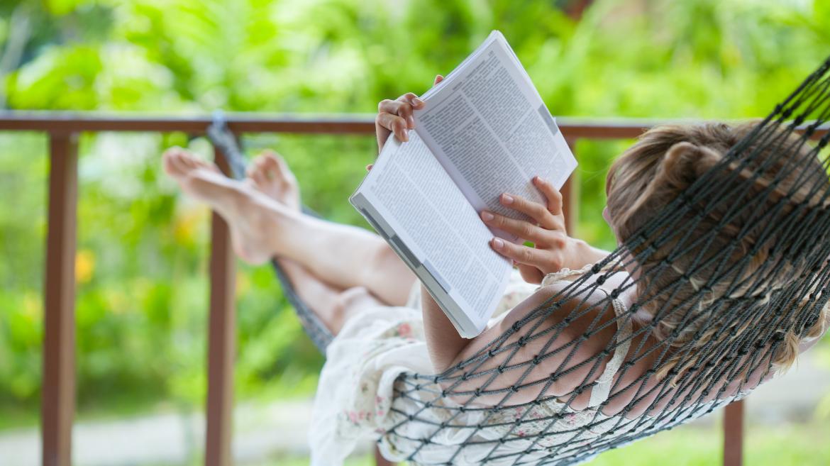 Mujer joven leyendo un libro tumbada en una hamaca