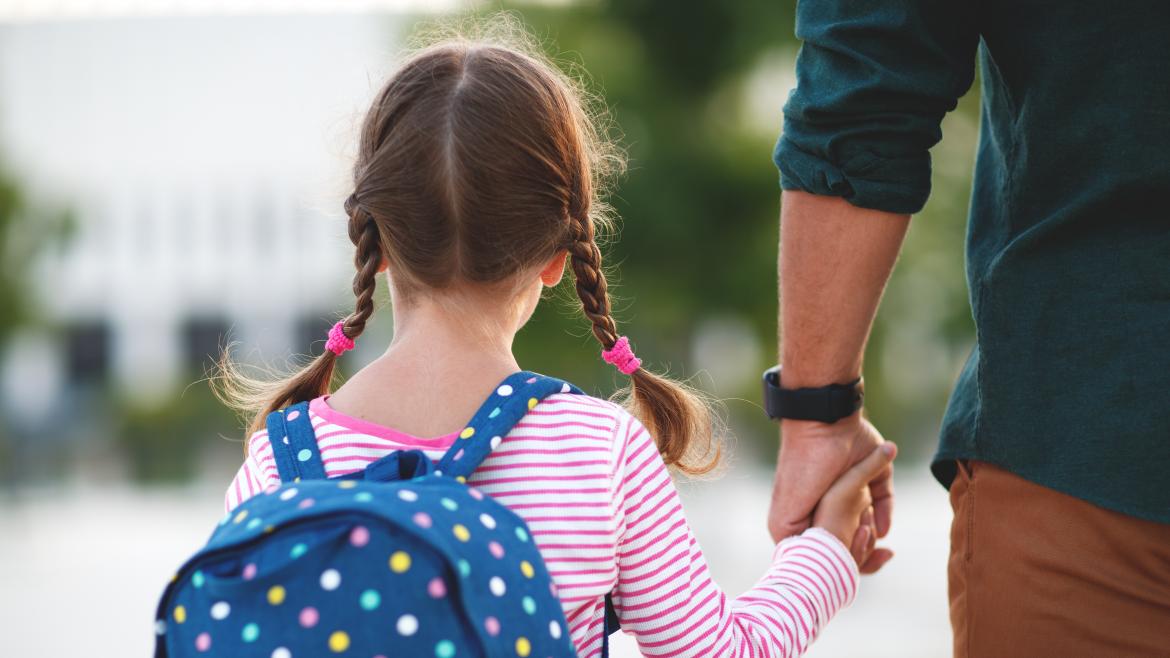 niña de espaldas cogida de la mano de una persona adulta