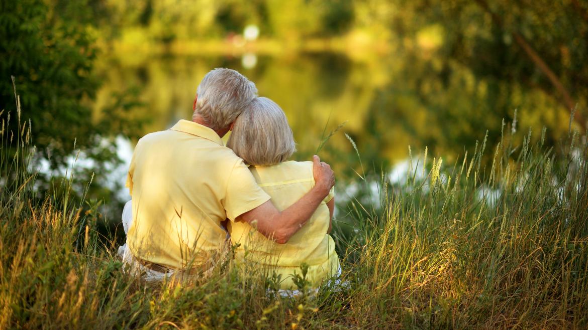Dos personas mayores abrazadas sentadas a los pies de un lago