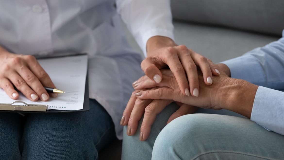 Una persona muestra su apoyo a otra colocando su mano sobre las suyas al tiempo que toma notas en una libreta