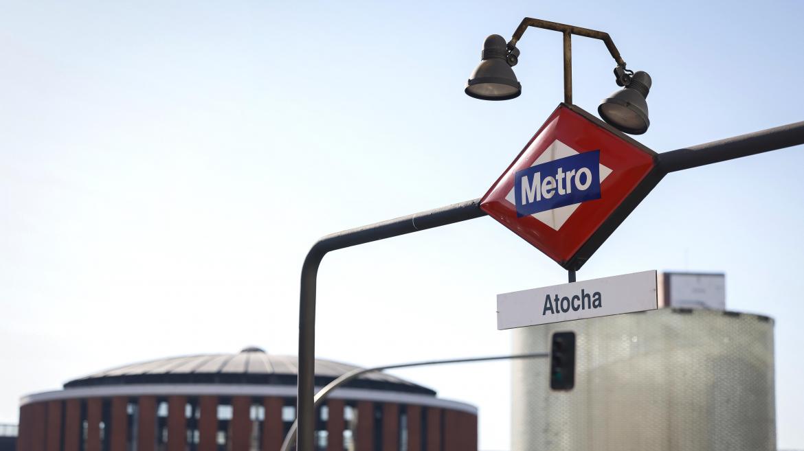 Cartel de metro con Atocha y de fondo la estación