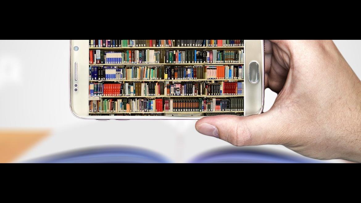 Movil con imagen de biblioteca en fondo, haciendo foto de un libro