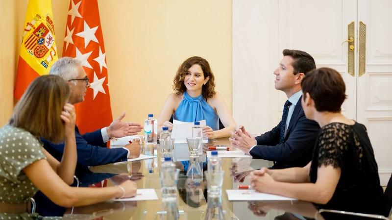 La presidenta sentada en la mesa de la reunión junto al resto de participantes