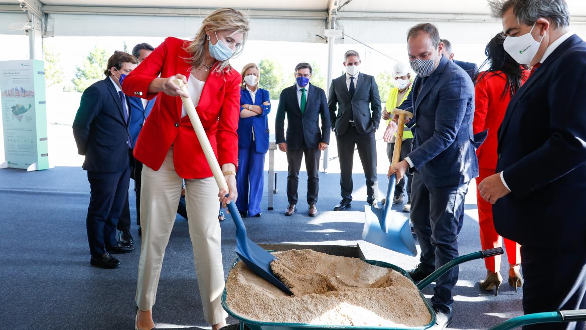La consejera con una pala cogiendo arena de una carretilla como símbolo de la colocación de esa primera piedra