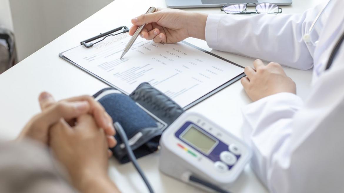 médico escribiendo en formulario con tensiómetro al lado y manos de paciente