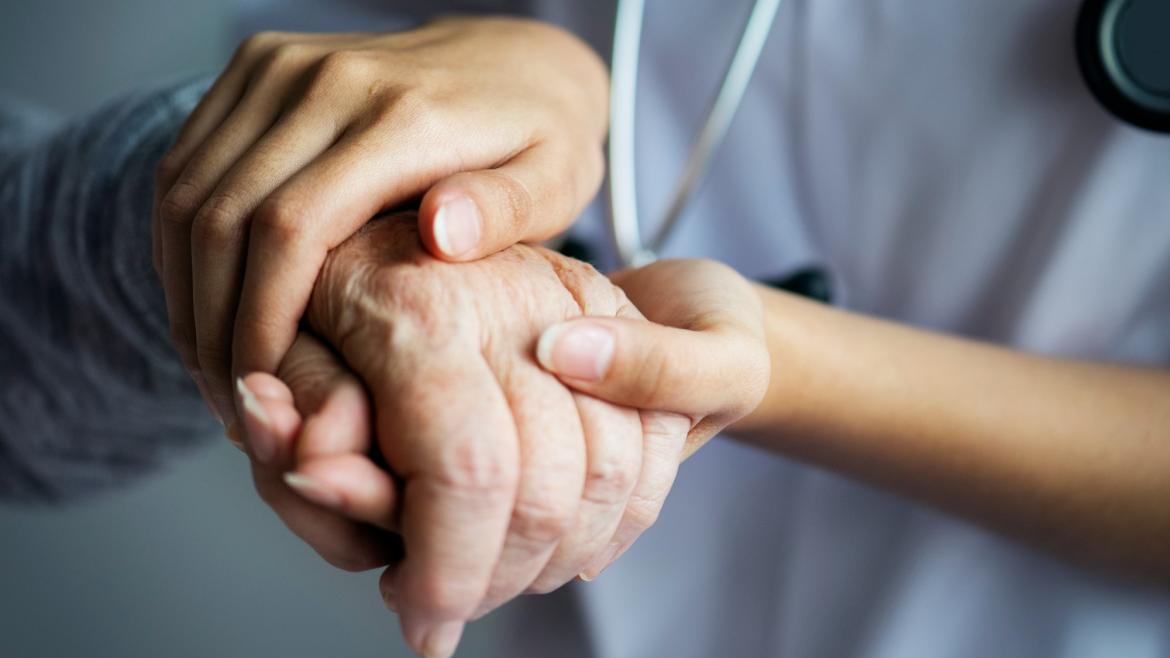 Un sanitario coge las manos de una persona mayor