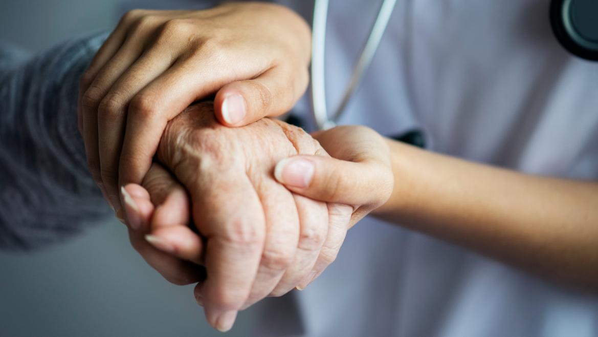 Un sanitario coge las manos de una persona mayor