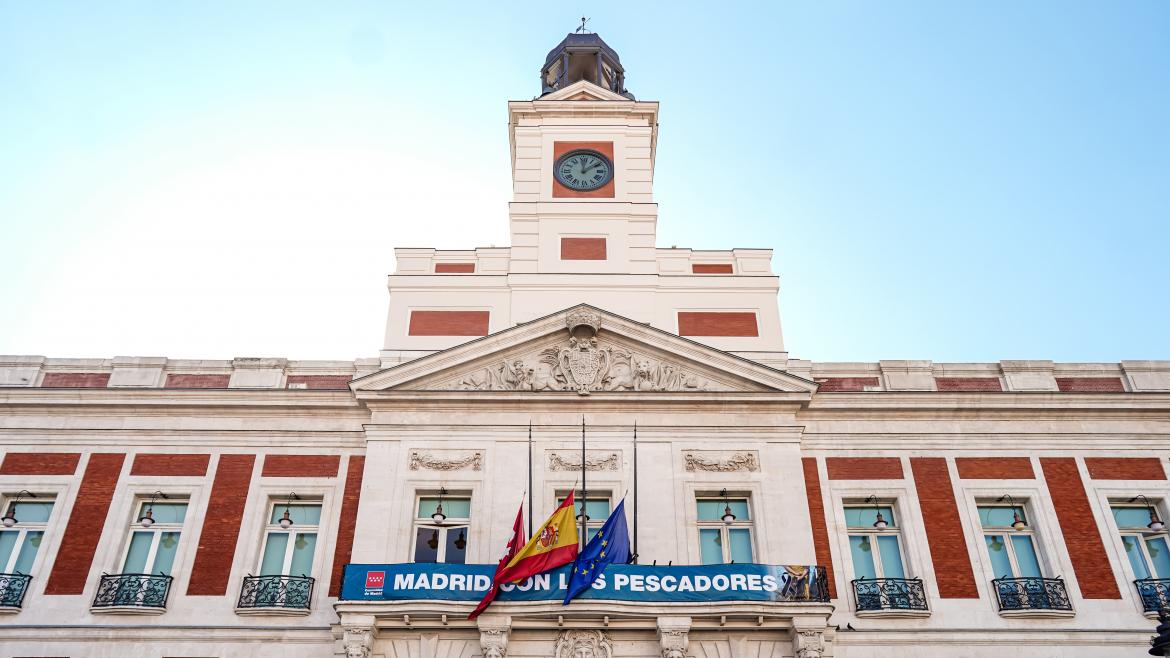 Vista de la fachada de la Real Casa de Correos con la pancarta del homenaje y las banderas a media asta