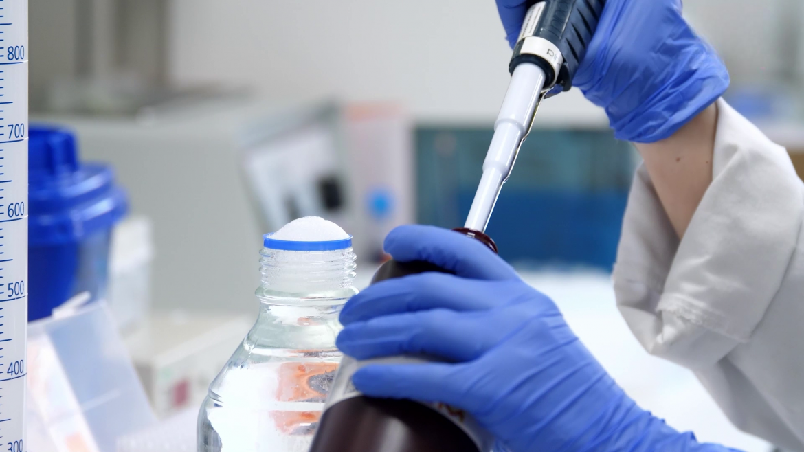 Laboratorio del Centro de Oncología Experimental del Hospital 12 de Octubre Manos de profesional con guantes azules con pipeta introduciendo líquiso en un frasco en laboratorio