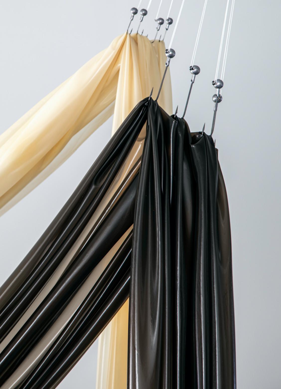 Dos tiras de latex, una negra y otra beiga, estiradas por ganchos