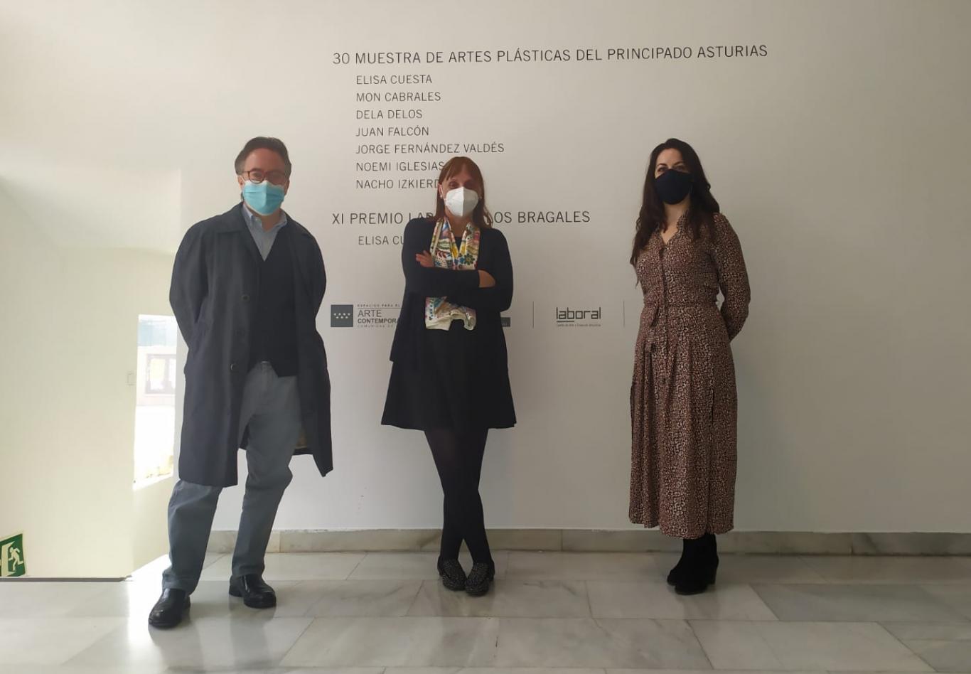 Tres personas frente a una pared con el titulo de la exposición "Muestra asturiana"